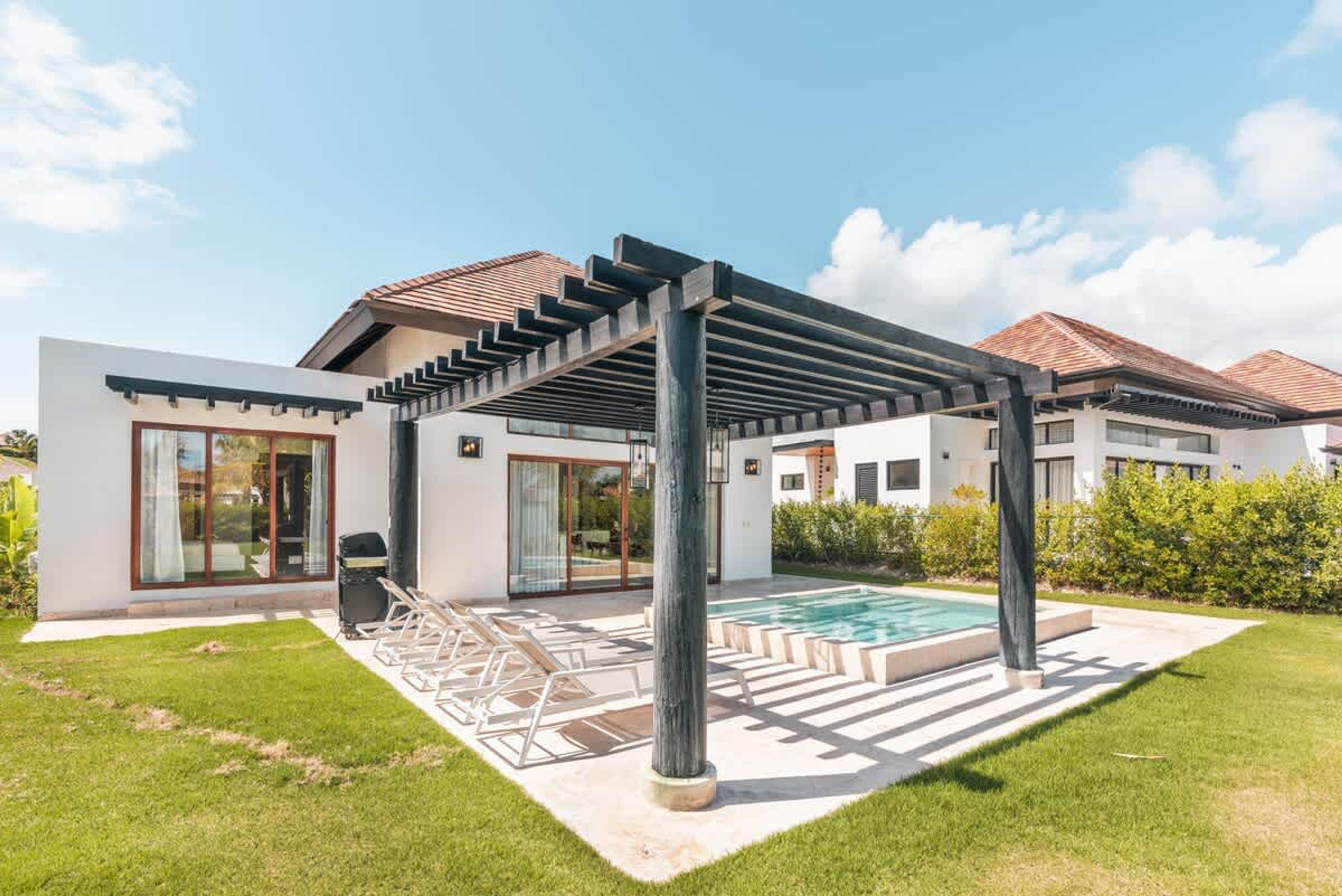 A modern house with a covered outdoor area, a swimming pool, and a well-maintained lawn.