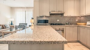 Cozinha moderna com bancadas de granito, eletrodomésticos de aço inoxidável e armários de madeira clara.