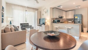 Uma cozinha moderna com uma ilha central, uma área de jantar com mesa redonda e uma sala de estar com sofá e poltrona estampada.