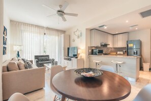 A modern kitchen with a central island, a dining area with a round table, and a living room with a sofa and a patterned armchair. - Exclusive 1br apt Nearby Beach at el Portillo Vc (Las Terrenas)