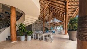 Um hall espaçoso com uma escadaria em curva, teto alto com cobertura trançada e área de estar com plantas em vasos.