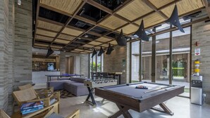 A pool table, sofas, and a foosball table in a modern indoor space with large windows and a brick wall. - 2br 5 Guests Private Balcony and Shared Pool (Cartagena)