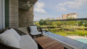 A balcony with wicker furniture, a ceiling fan, and a view of a swimming pool and greenery. - 2br 5 Guests Private Balcony and Shared Pool (Cartagena)