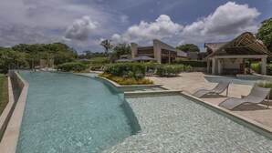 A swimming pool area with lounge chairs, a covered seating area, and a building with a modern architectural style. - 2br 5 Guests Private Balcony and Shared Pool (Cartagena)
