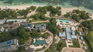 Vista aérea de un complejo turístico con varias construcciones, una piscina y una playa.