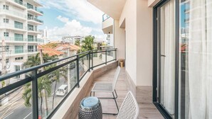 A balcony with a view of palm trees, a white chair, a small table, and a glass railing. - Flat in Piantini 302 (Santo Domingo)