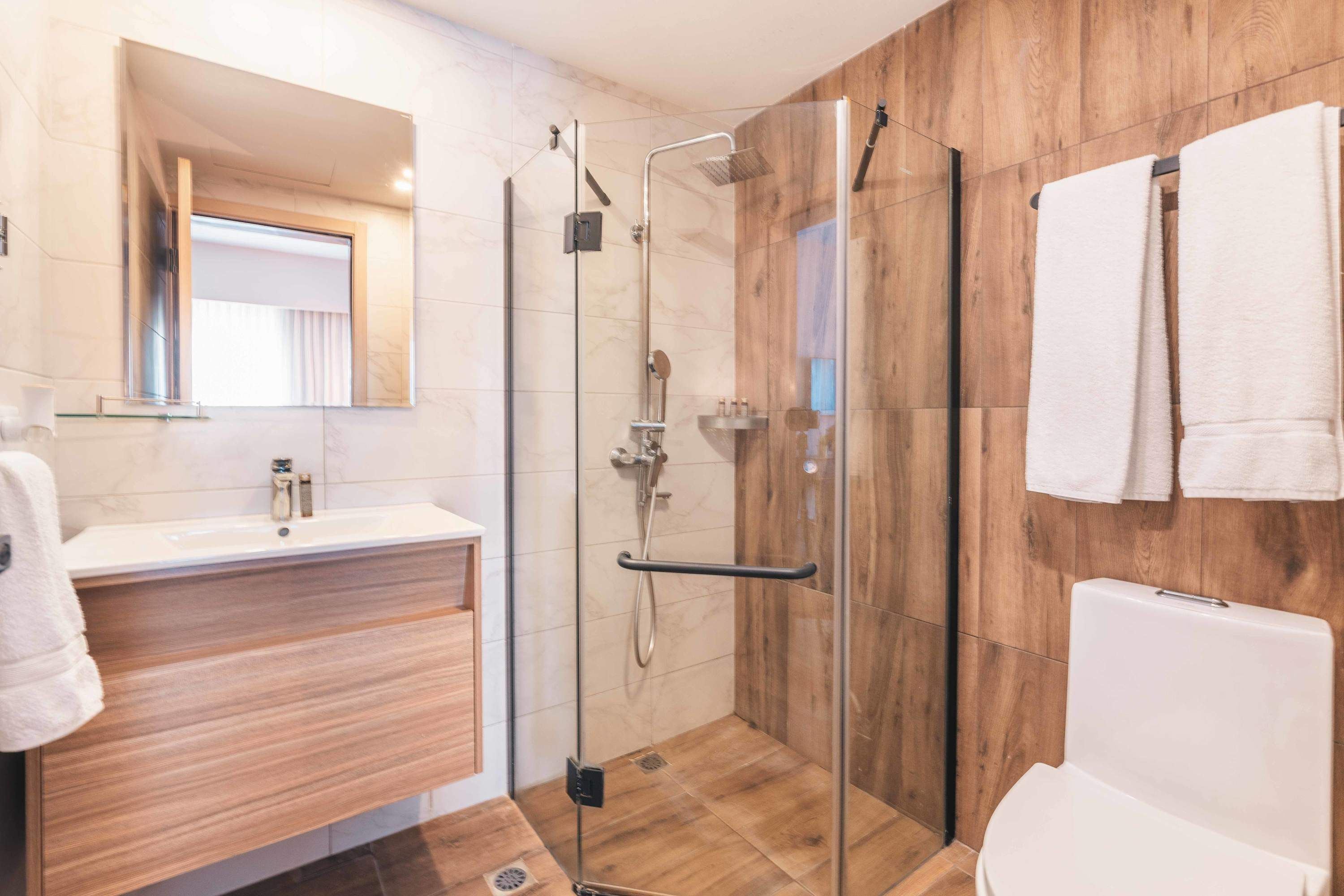 Un bany modern amb dutxa de vidre, un tocador de fusta, un lavabo blanc i un vàter.