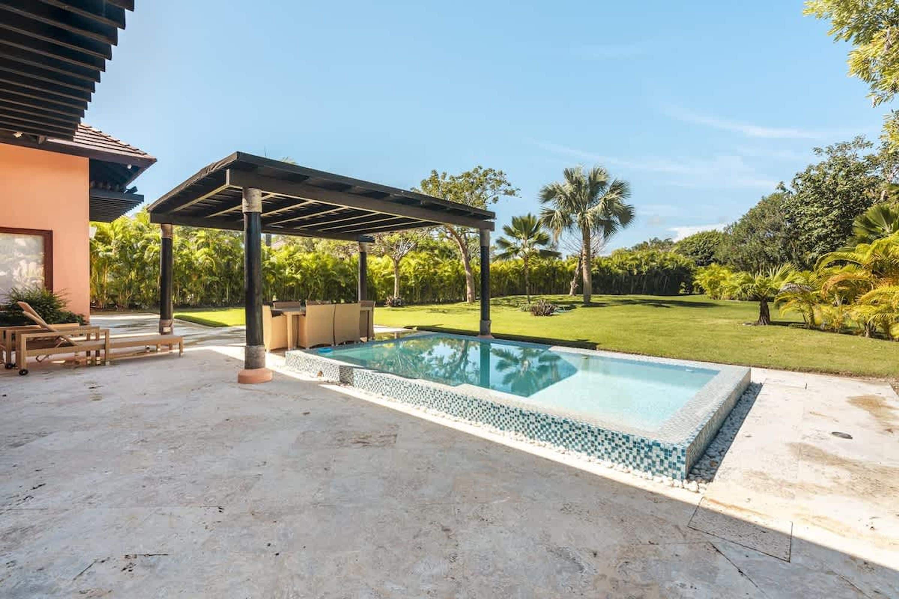 Ein Pool im Freien mit einer Pergola, Liegestühlen und einem gepflegten Rasen.