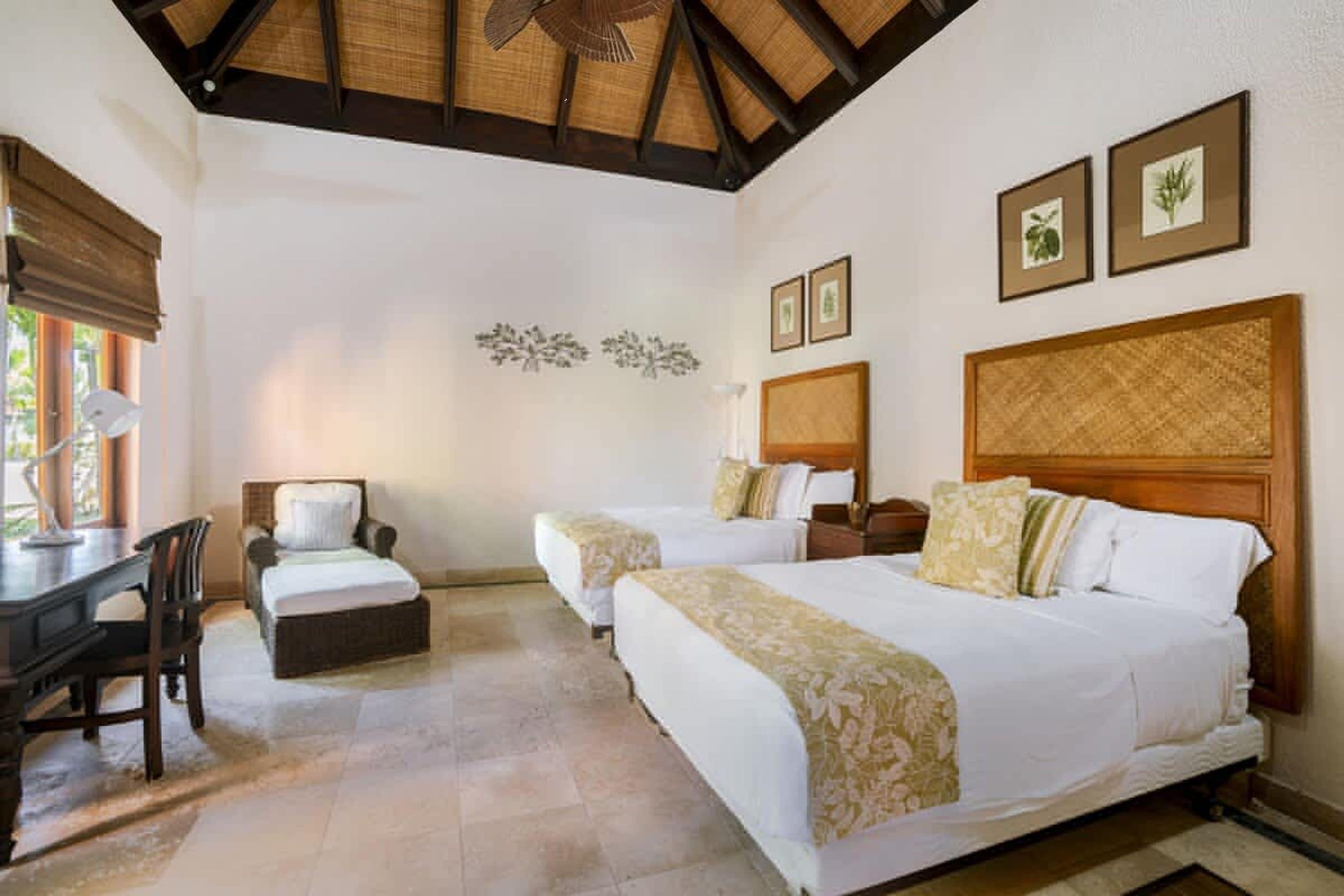 A hotel room with two beds, a desk, a chair, and a ceiling fan.