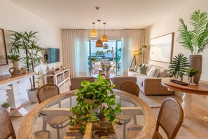 Un salon moderne avec une table à manger au plateau en verre, des meubles en osier et des plantes en pot.