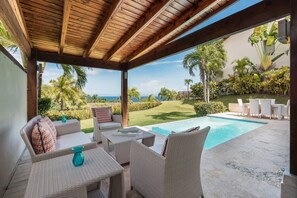 Uma área externa coberta com móveis de vime, piscina e vista para o oceano.