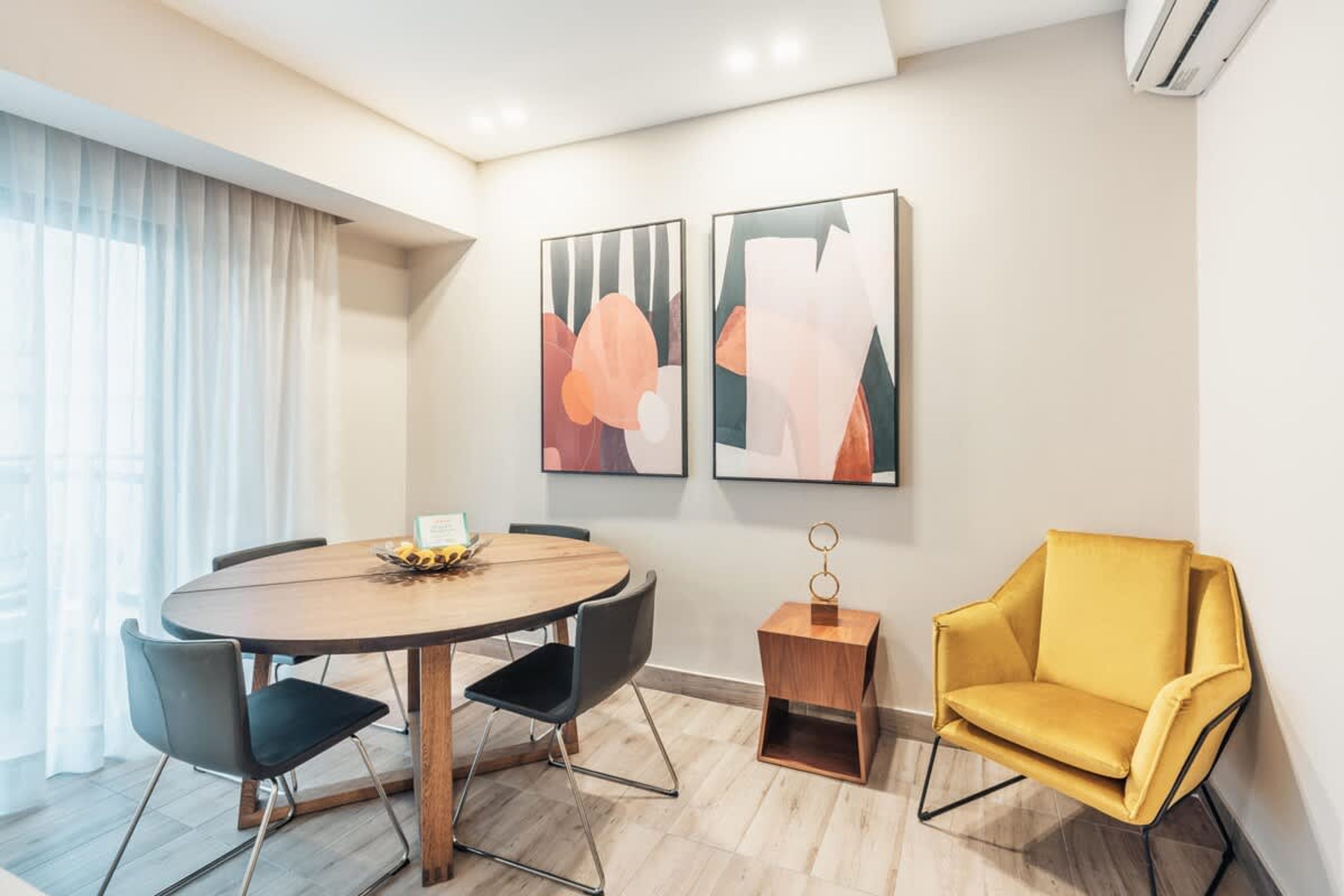 A modern room with a round table, four chairs, a yellow armchair, and abstract art on the wall.