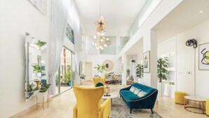 Ein geräumiger Wohnbereich mit hoher Decke, einem blauen Sofa, einem gelben Sessel und einem großen Spiegel.