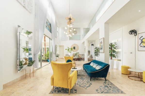 A spacious living area with a high ceiling, a blue sofa, a yellow armchair, and a large mirror.