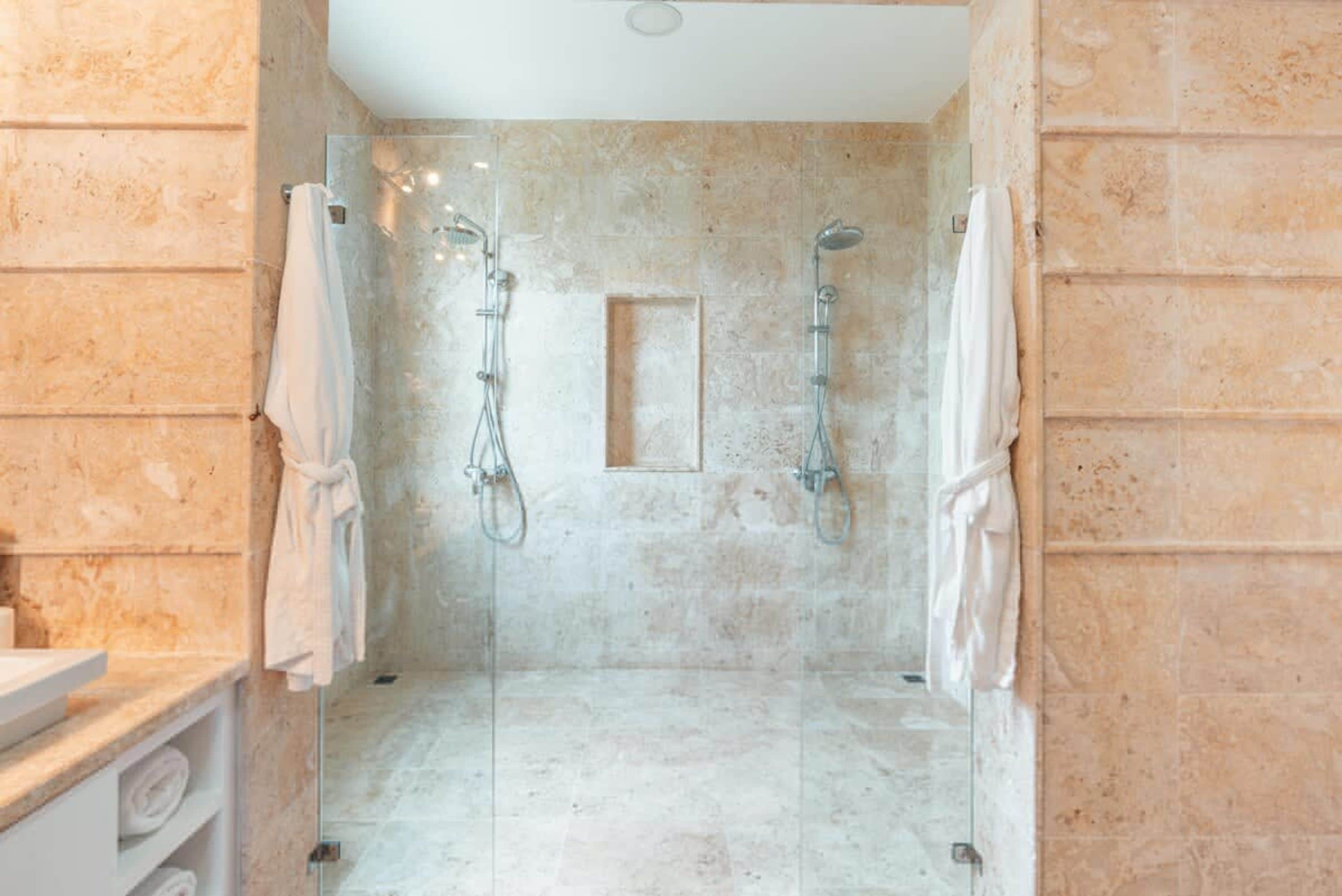 Een moderne badkamer met een douchecabine van glas, marmeren wanden en een inbouwwastafel.