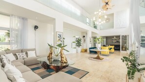 Ein großzügiger Wohnbereich mit Ecksofa, Couchtisch und Esstisch. An den Wänden befinden sich Pflanzen und Kunstwerke, im Hintergrund ist ein Balkon zu sehen.