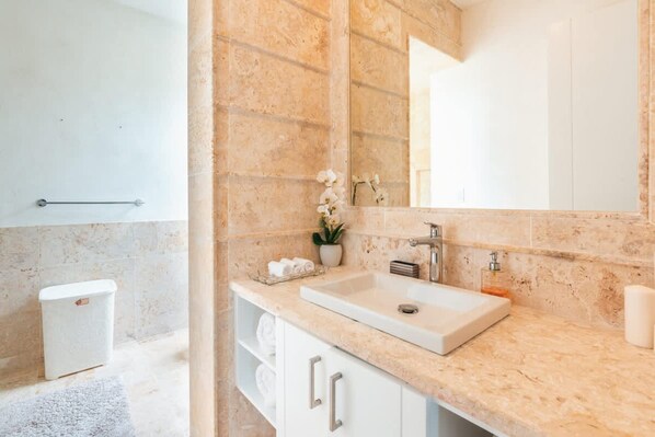 A bathroom with a marble sink, a large mirror, a towel rack, and a trash bin.