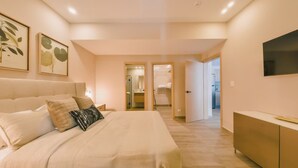A bedroom with a bed, bedside tables, a wardrobe, and a TV. There are framed pictures on the wall and a door leading to a bathroom. - Regatta Living Ii - 703 (Santo Domingo)