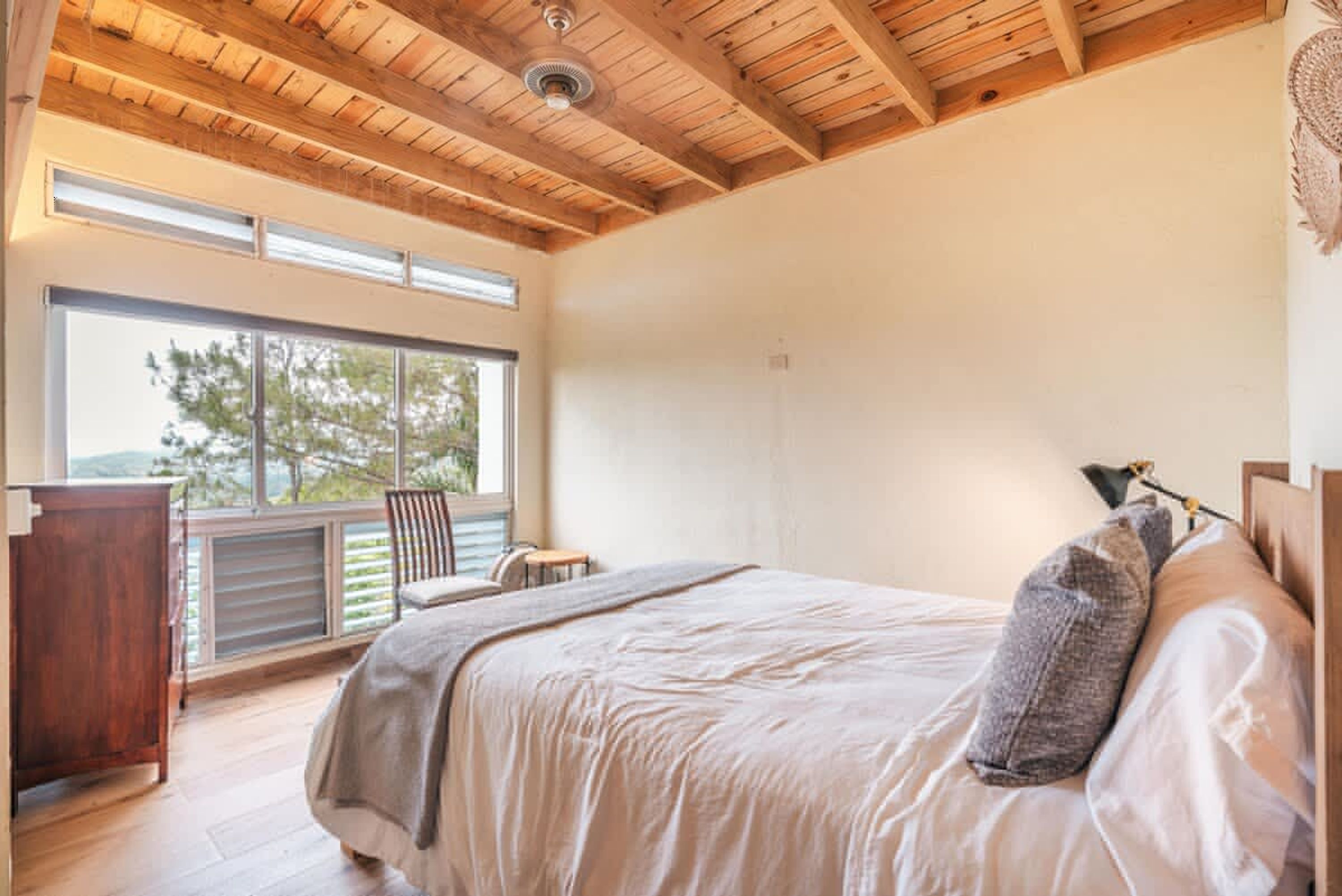 Une chambre avec un grand lit, un plafond en bois, une fenêtre et une chaise.