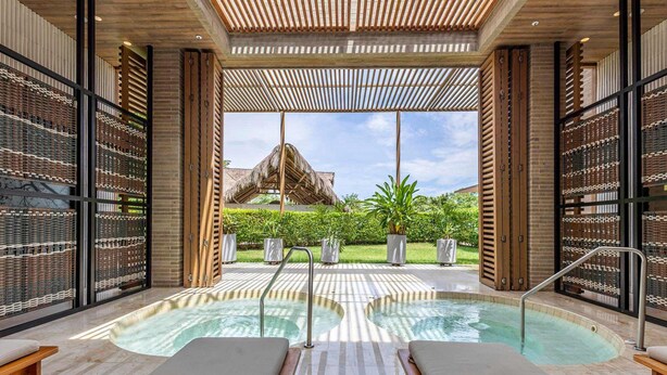A spa area with a hot tub, lounge chairs, and a view of a thatched-roof structure. - 3-bedroom Apartment With Ocean Views in Baru (Cartagena)