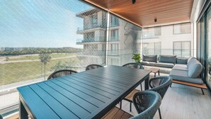 Ein Balkon mit Tisch, Stühlen, einer Sitzecke und Blick auf ein Gebäude und Grünflächen.