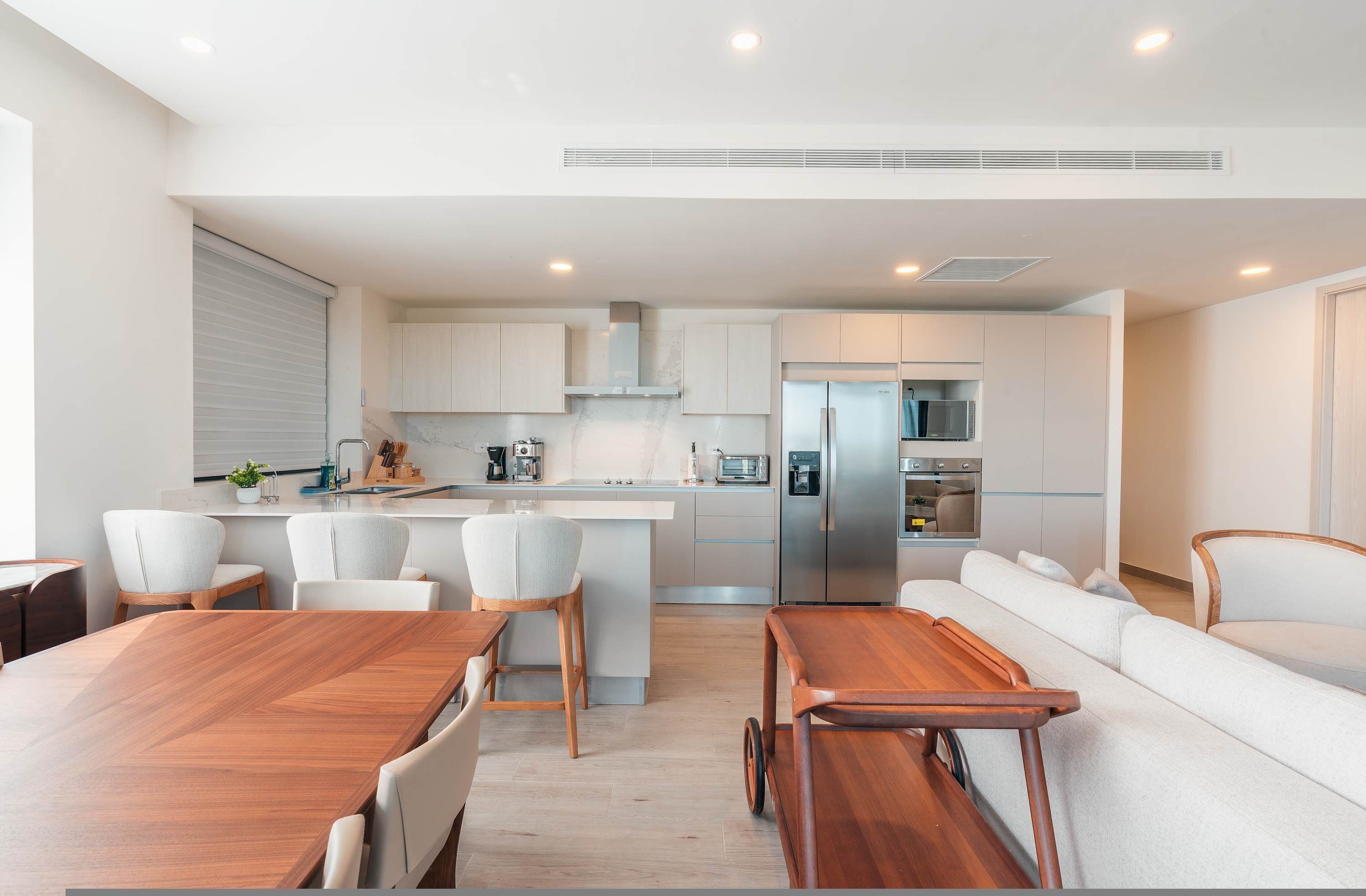 A modern kitchen with a central island, white cabinetry, stainless steel appliances, and a dining area with a wooden table and chairs.
