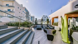 Eine Dachterrasse mit Außenmöbeln, Treppenaufgang und Blick auf die umliegenden Gebäude.