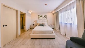 Ein Schlafzimmer mit einem großen Bett, Nachttischen, einem Beistelltisch, einem Sessel und einem Fenster mit Vorhängen.