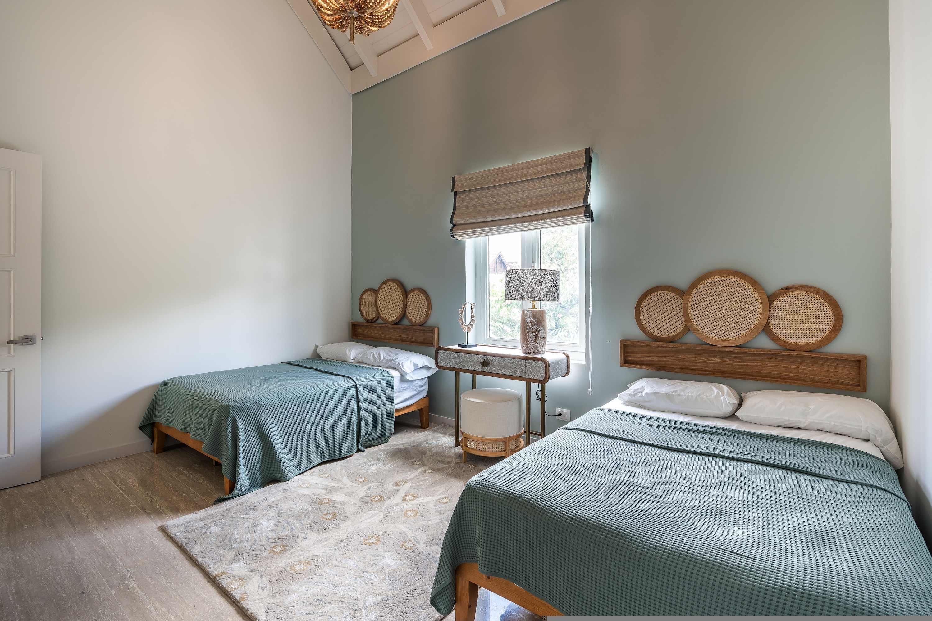 A bedroom with two beds, a window with a blind, a bedside table, and a rattan headboard.