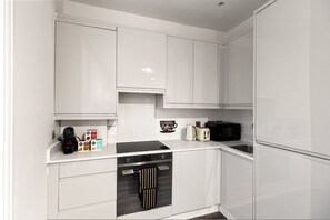 A modern kitchen with white cabinetry, a built-in oven, a microwave, and a coffee machine. - Cozy 2-bedroom Flat in Central London (London)