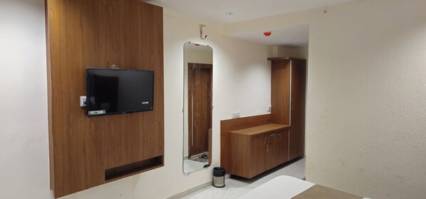 A modern bathroom with a wooden vanity, a mirror, a television mounted on the wall, and a white bathtub.