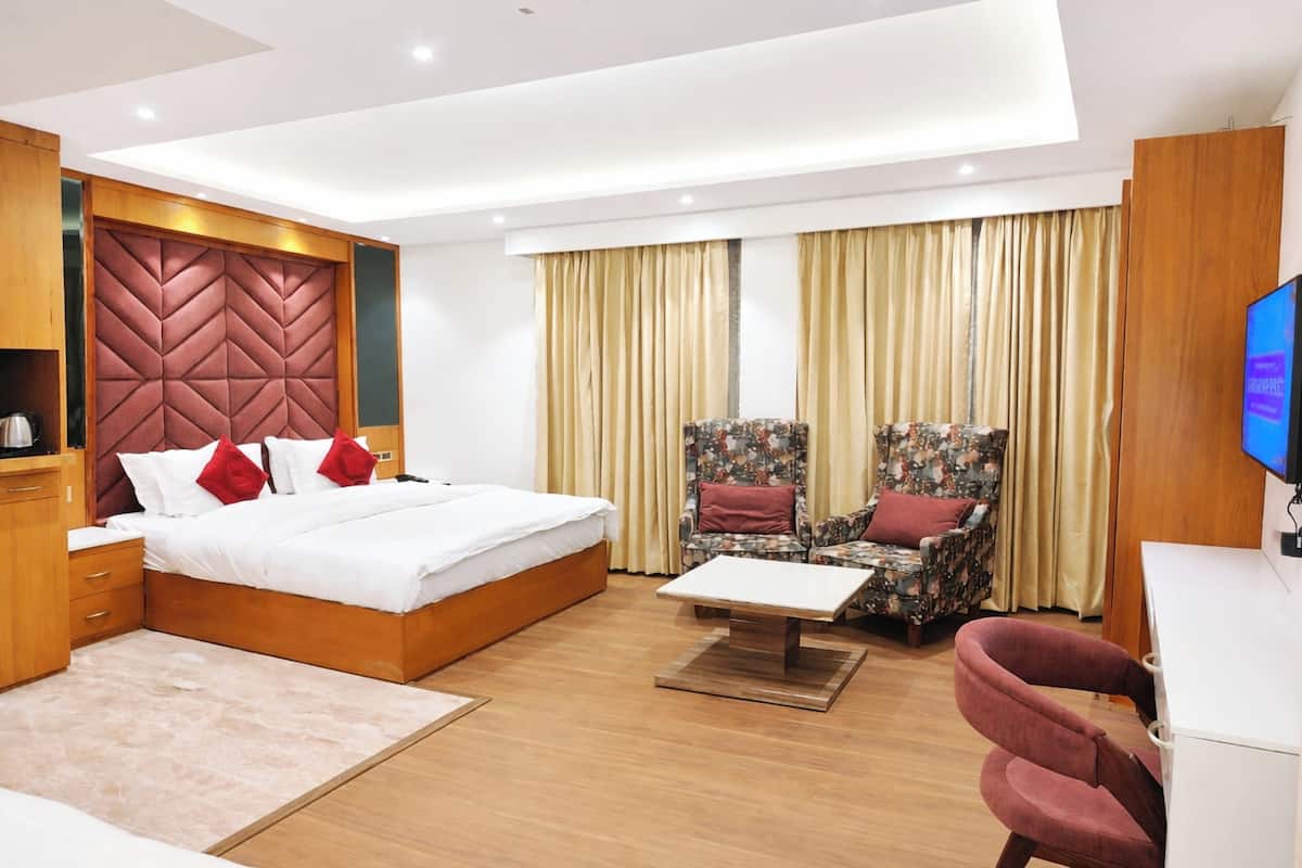 Ein modernes Hotelzimmer mit einem großen Bett, einem Schreibtisch, zwei Sesseln, einem Fernseher und einem dekorativen Kopfteil.