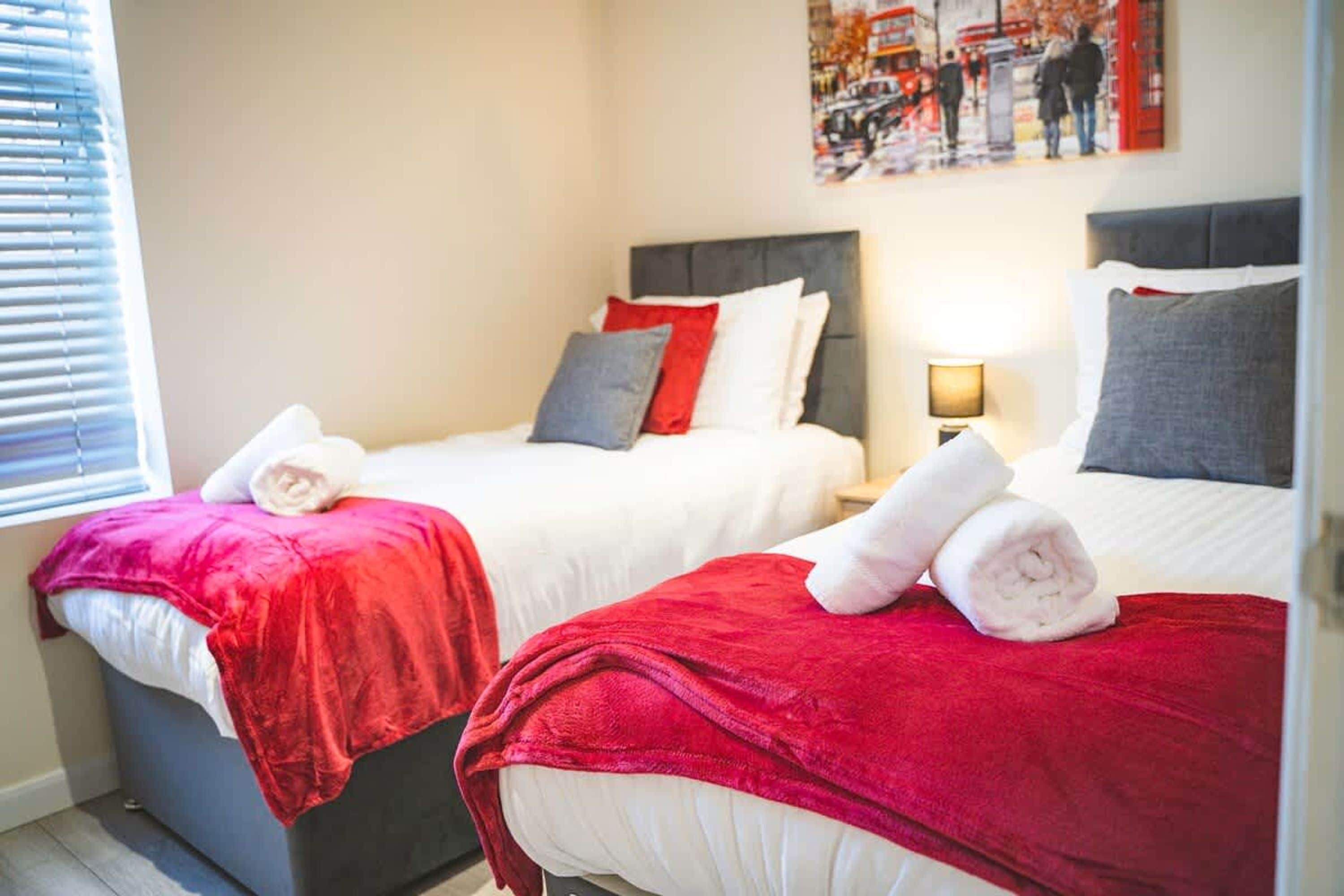 Two beds with red and white bedding, a nightstand with a lamp, and a painting on the wall.