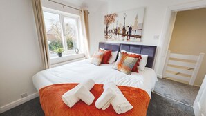 A bedroom with a large bed, a window with curtains, a painting of a cityscape, and a white door. - Spacious Home Ideal For Families Free Parking (Chester)