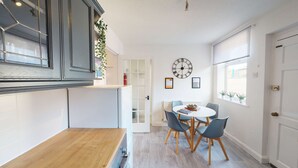 A modern kitchen with dark cabinets, a white countertop, and a dining area with a round table and chairs. - Spacious Home Ideal For Families Free Parking (Chester)