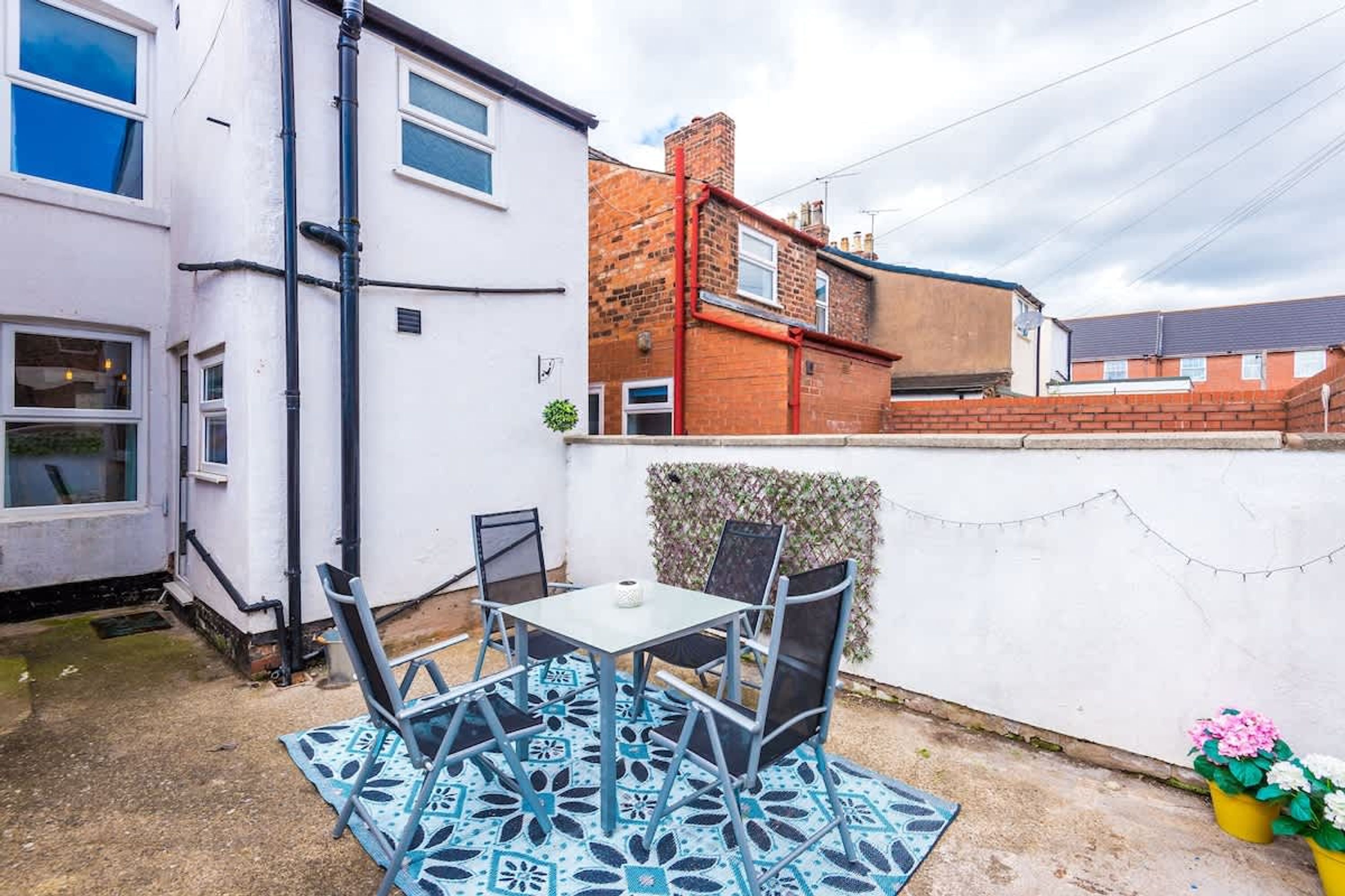 A patio with a table and chairs, a white building, and a brick wall.