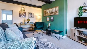 A living room with a sofa, a chair, a TV, and a painting on the wall. - Cosy House Amazing Location Perfect for Couples (Chester)