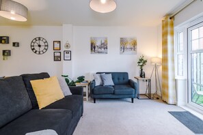 A living room with a sofa, a smaller couch, a side table with a lamp, a clock, and framed pictures on the wall. - Spacious Home Ideal for Professionals Sleeps 8 (Crewe)