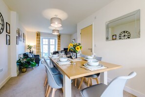 Un comedor con una mesa de madera dispuesta para cuatro personas, un sofá y un espejo grande en la pared.