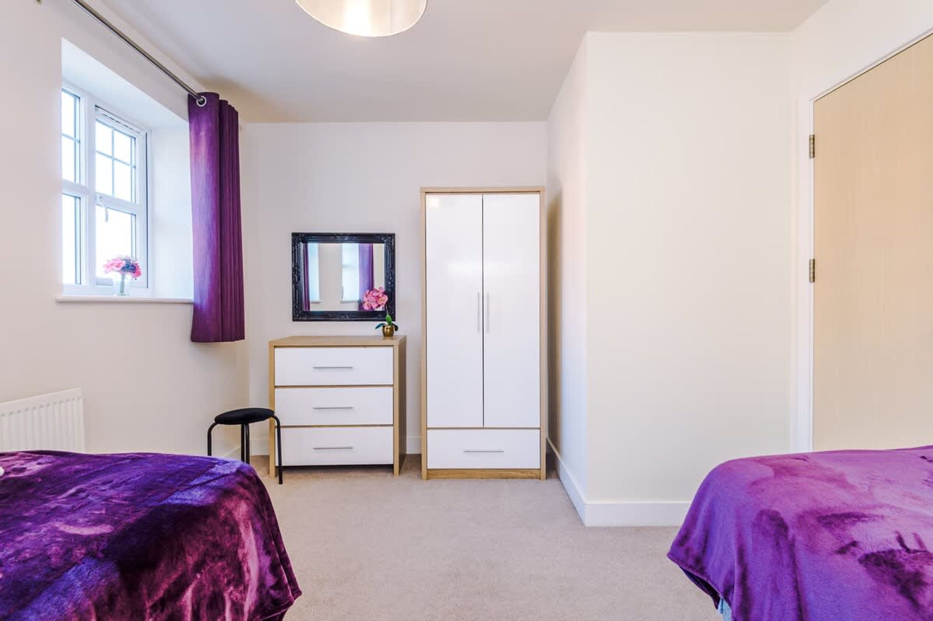 A bedroom with two beds, a dresser, a wardrobe, a mirror, and a window with curtains.