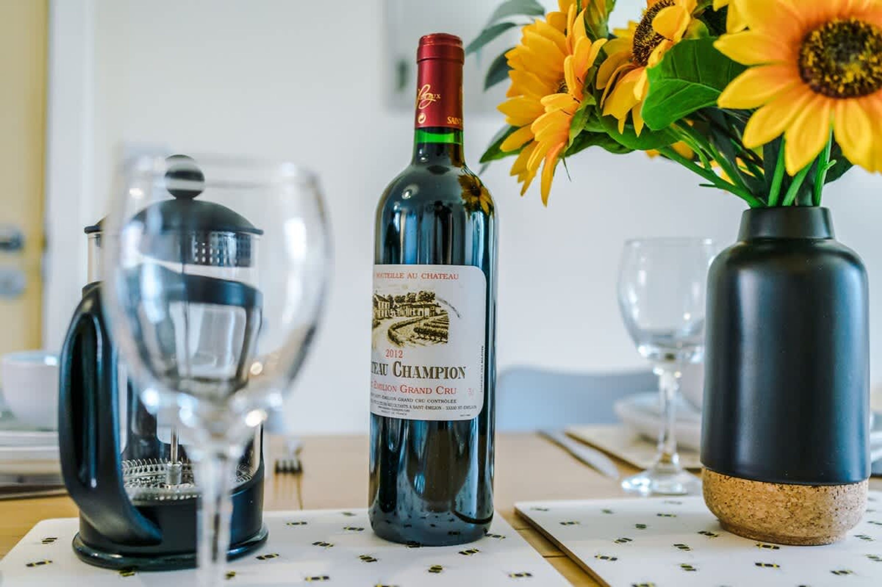 A bottle of wine, a coffee maker, and a vase with sunflowers on a table.