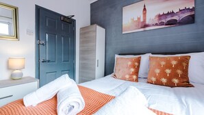 Ein Hotelzimmer mit einem Bett, einer blauen Tür, einem weißen Nachttisch mit Lampe und einem Gemälde einer Brücke.