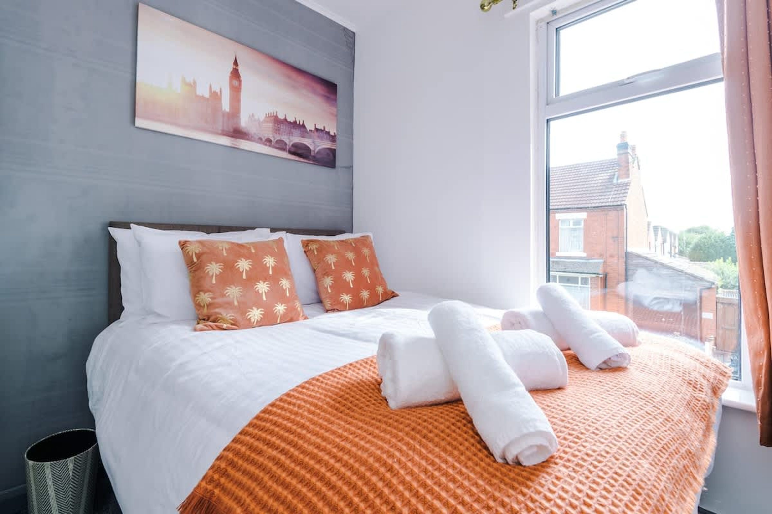 A hotel room with a bed, pillows, a blanket, and a painting of a cityscape.
