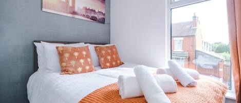 A hotel room with a bed, pillows, a blanket, and a painting of a cityscape.