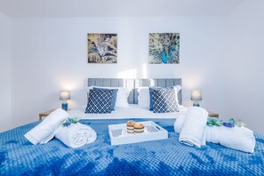 Une chambre d’hôtel avec un lit, deux lampes fixées au mur, un plateau de pâtisseries et des serviettes.