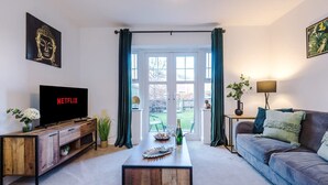 Ein Wohnzimmer mit Fernseher, Couch, Holztisch und Blick durch eine Glastür.