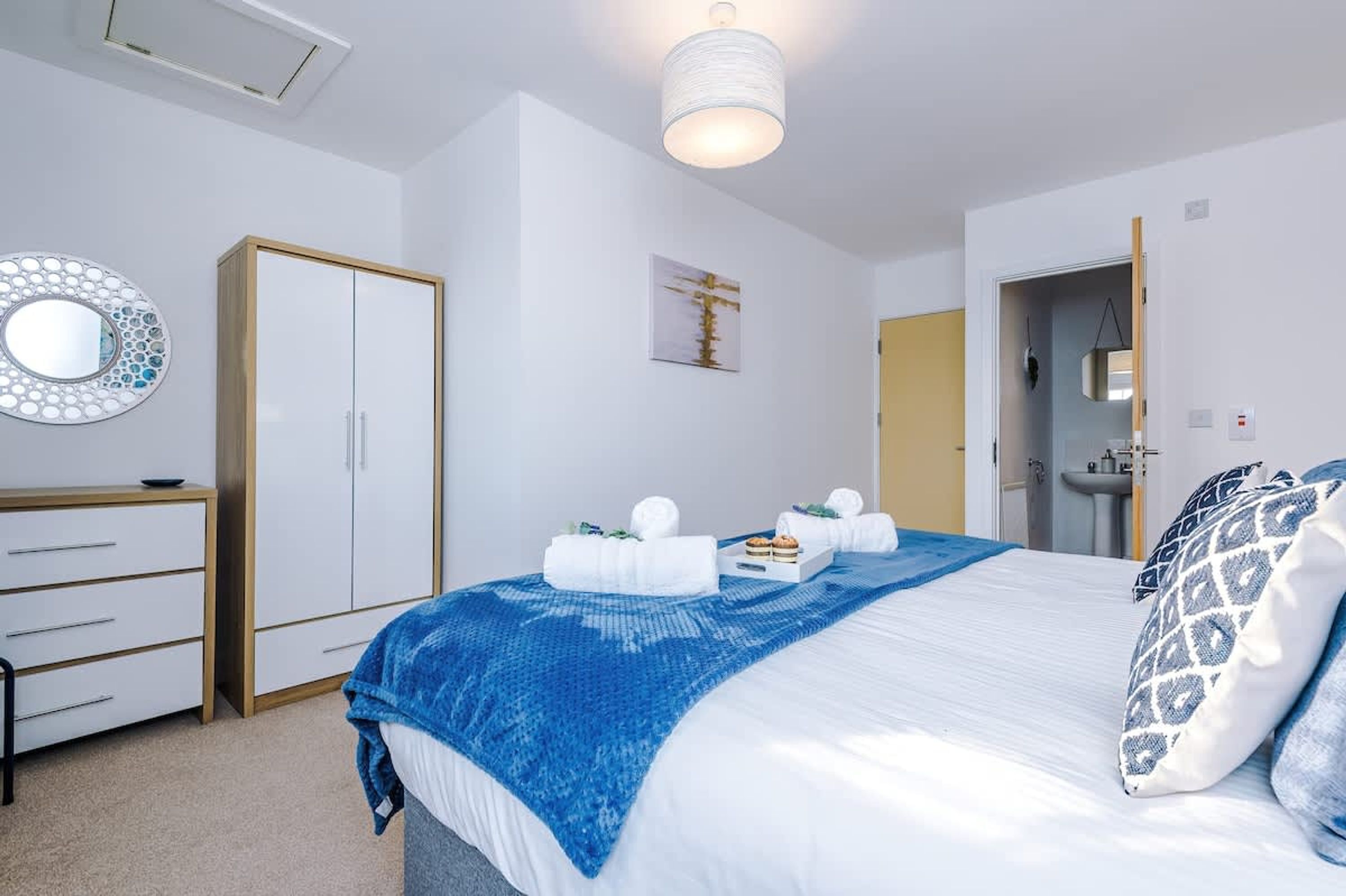 Ein Schlafzimmer mit Bett, Kleiderschrank, Spiegel, einem Gemälde und einer Badezimmertür.