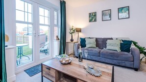 Ein Wohnzimmer mit einem grauen Sofa, einem Holztisch und Blick durch große Fenster.
