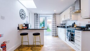 A modern kitchen with a central island, bar stools, a clock, and a view to the outside. - Stunning Home Perfect for Groups Free Parking (Chester)