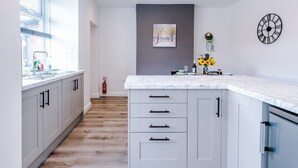Una cocina moderna con armarios blancos, encimera de mármol y un reloj montado en la pared.